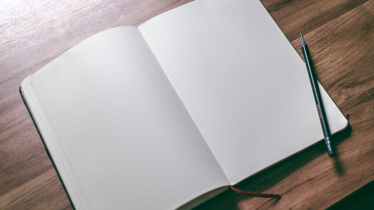 An open blank notebook and a pencil resting on a dark wooden desk