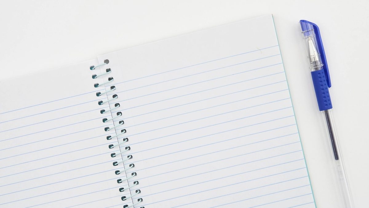 An open spiral notebook with lined pages and a blue pen on a white desk